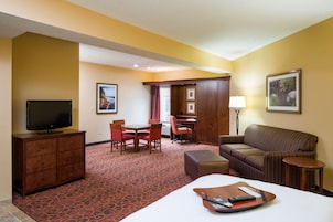 Habitación de hotel con cama, televisión, escritorio, silla, sofá y una pequeña mesa.