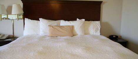 A neatly made bed with a wooden headboard, white pillows, and a beige throw pillow.