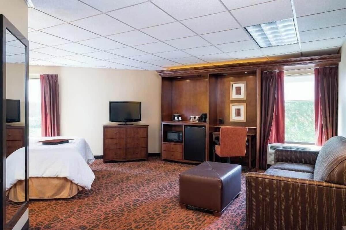 Una habitación de hotel con cama, televisión, escritorio, silla y ventana con cortinas.