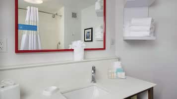 A hotel bathroom with a white sink, a mirror with a red frame, and shelves with towels.