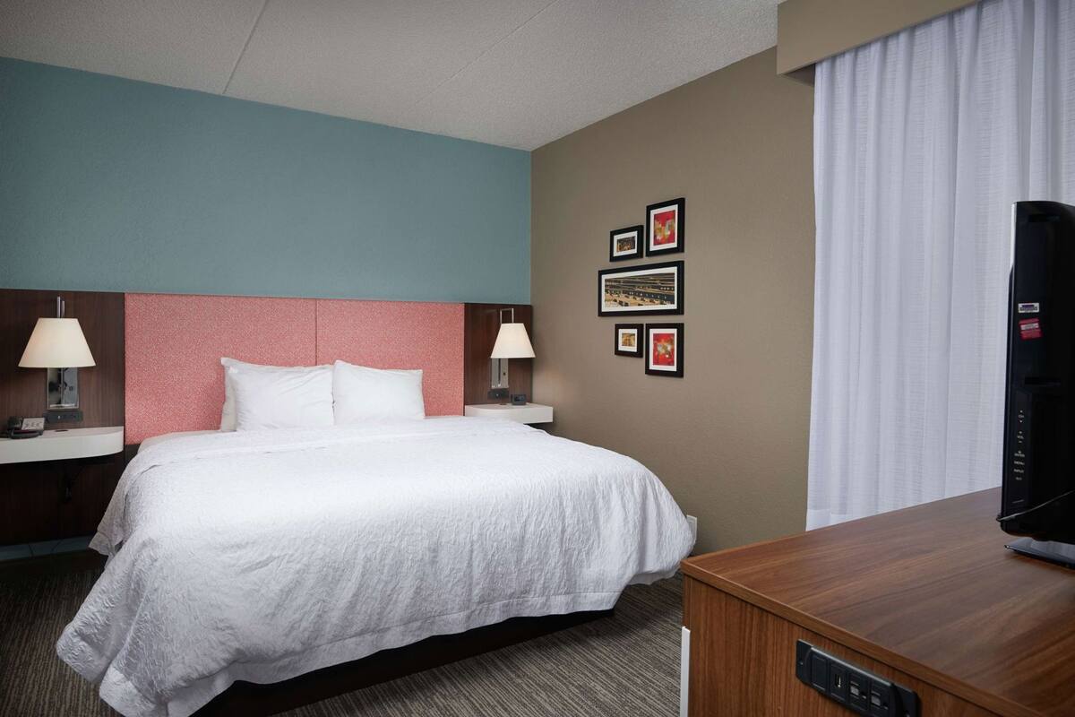Una habitación de hotel con una cama, dos mesitas de noche con lámparas, un televisor y una pared decorada con cuadros.