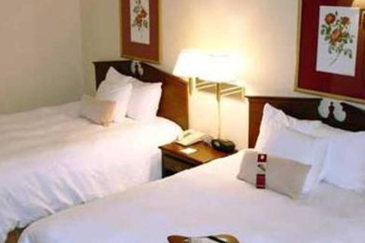 Una habitación de hotel con dos camas, una mesita de noche con lámpara y cuadros en las paredes.