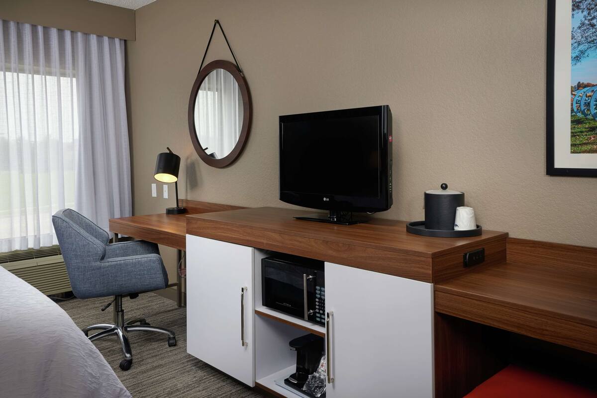 Una habitación de hotel con un escritorio de madera, televisión, silla, microondas y cafetera.