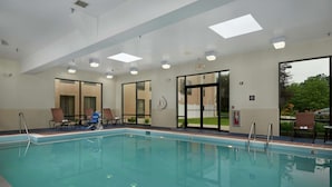 Una gran piscina interior con agua cristalina, rodeada de puertas y ventanas de vidrio, y equipada con múltiples luces en el techo.