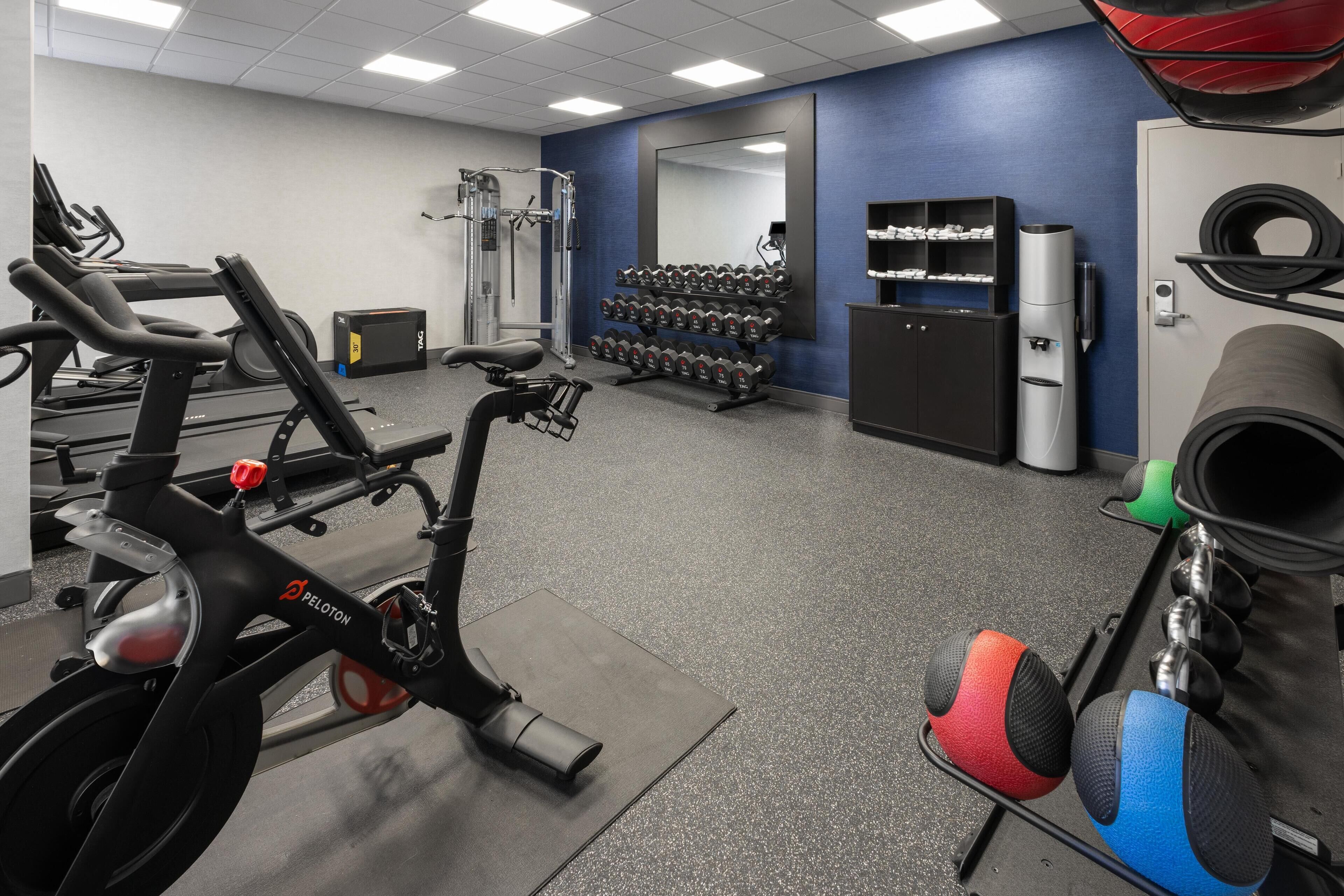 A gym with exercise equipment, a treadmill, dumbbells, and a water dispenser.