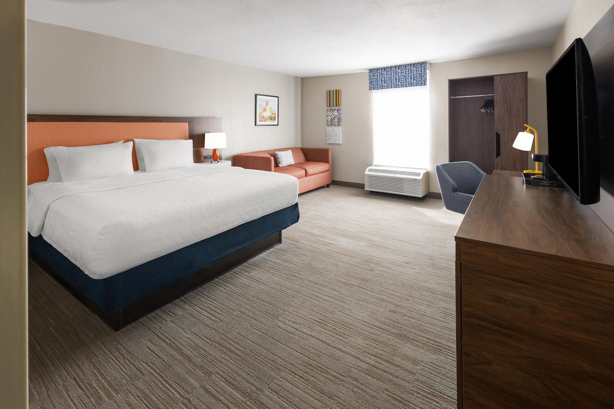 A hotel room with a large bed, a desk with a TV, a sofa, and a wardrobe.
