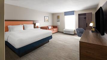 A hotel room with a large bed, a desk with a TV, a sofa, and a wardrobe.