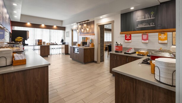 A modern hotel kitchen with wooden counters, a central island, and various breakfast items.