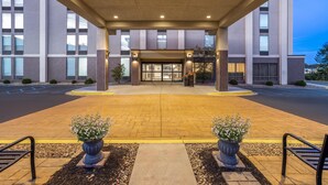 A modern hotel entrance with a covered walkway, large windows, and potted plants.