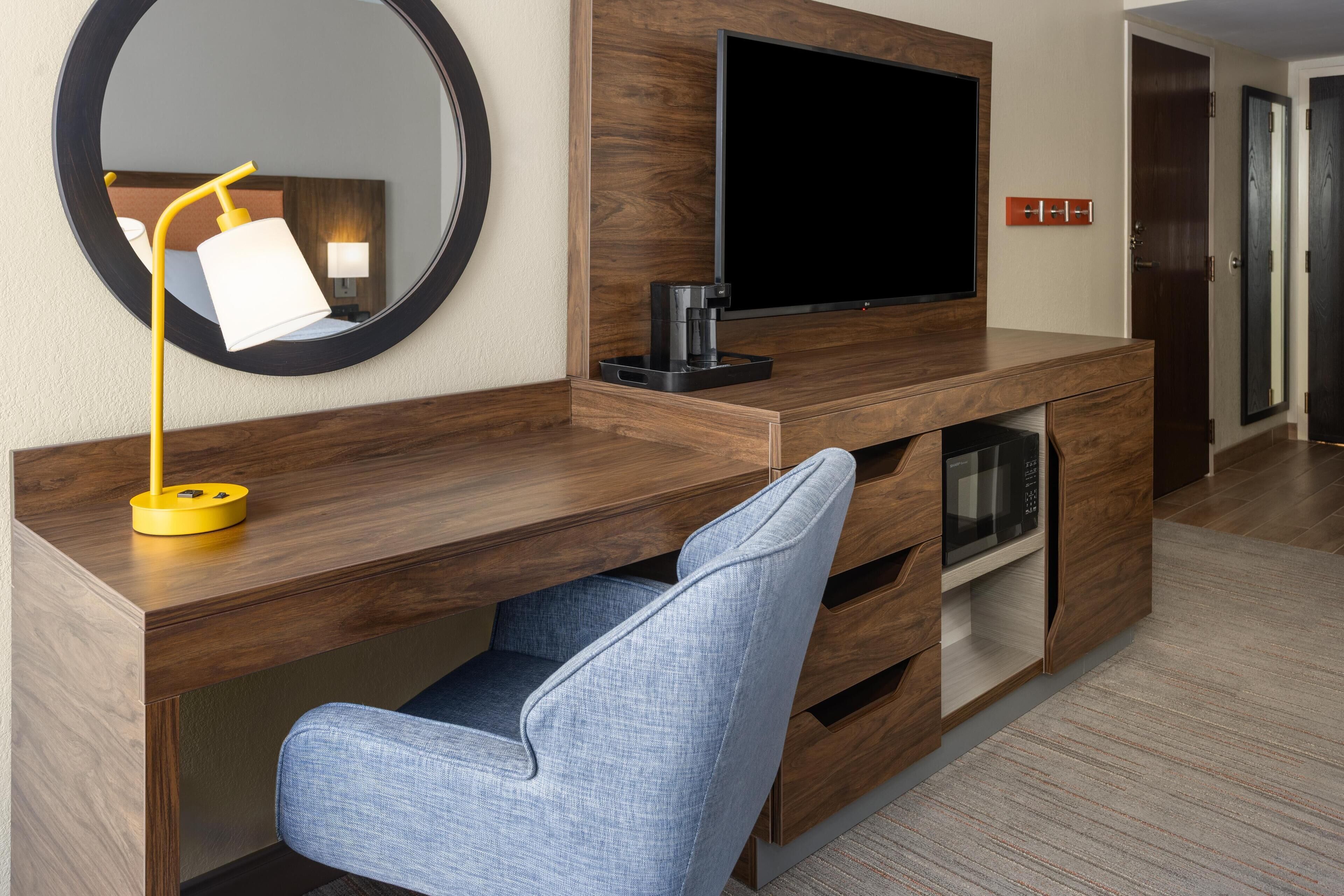 A modern hotel room with a wooden desk, a flat-screen TV, a coffee maker, and a built-in microwave.