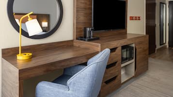 A modern hotel room with a wooden desk, a flat-screen TV, a coffee maker, and a built-in microwave.