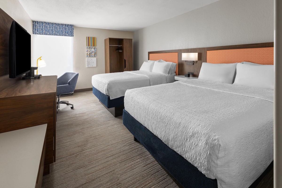 A hotel room with two beds, a desk, a TV, and a chair.