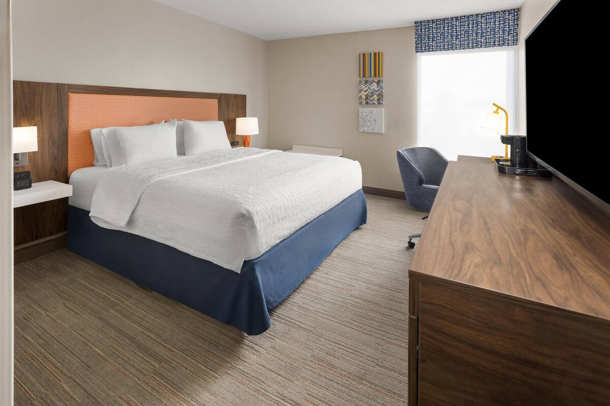 A hotel room with a bed, bedside tables, a desk, a chair, and a television.