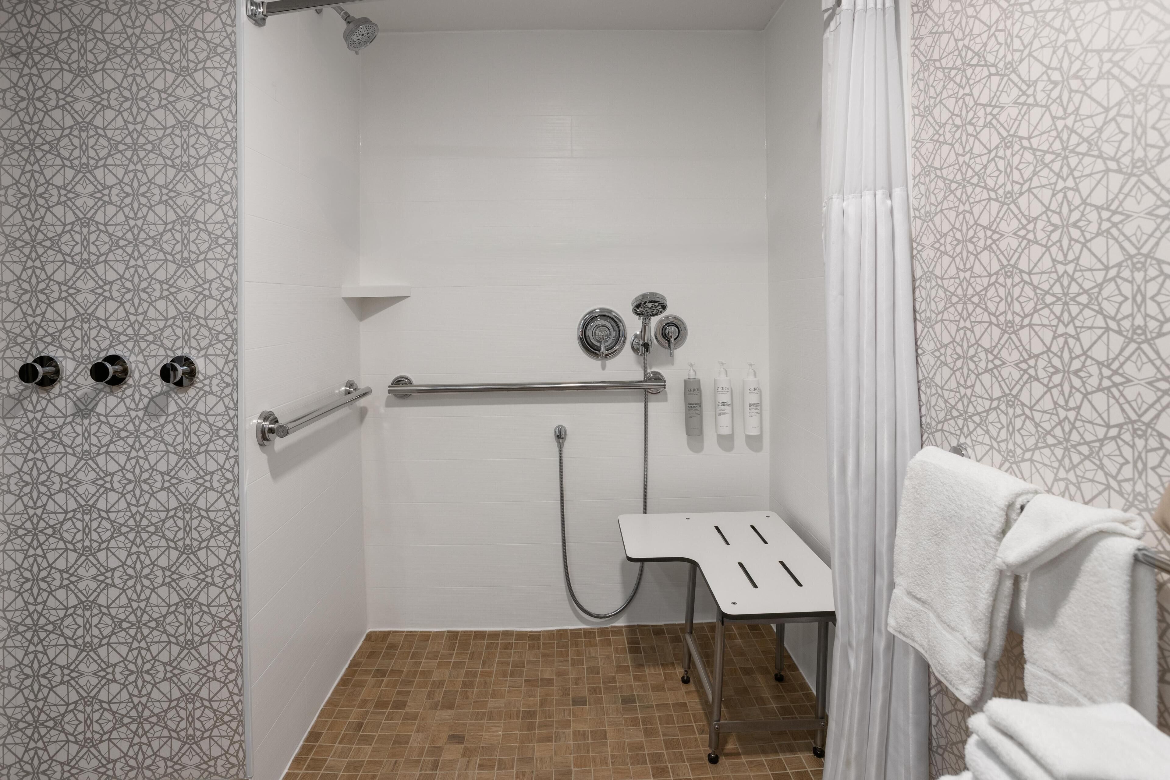 A shower area with a grab bar, a white towel rack, and a showerhead.