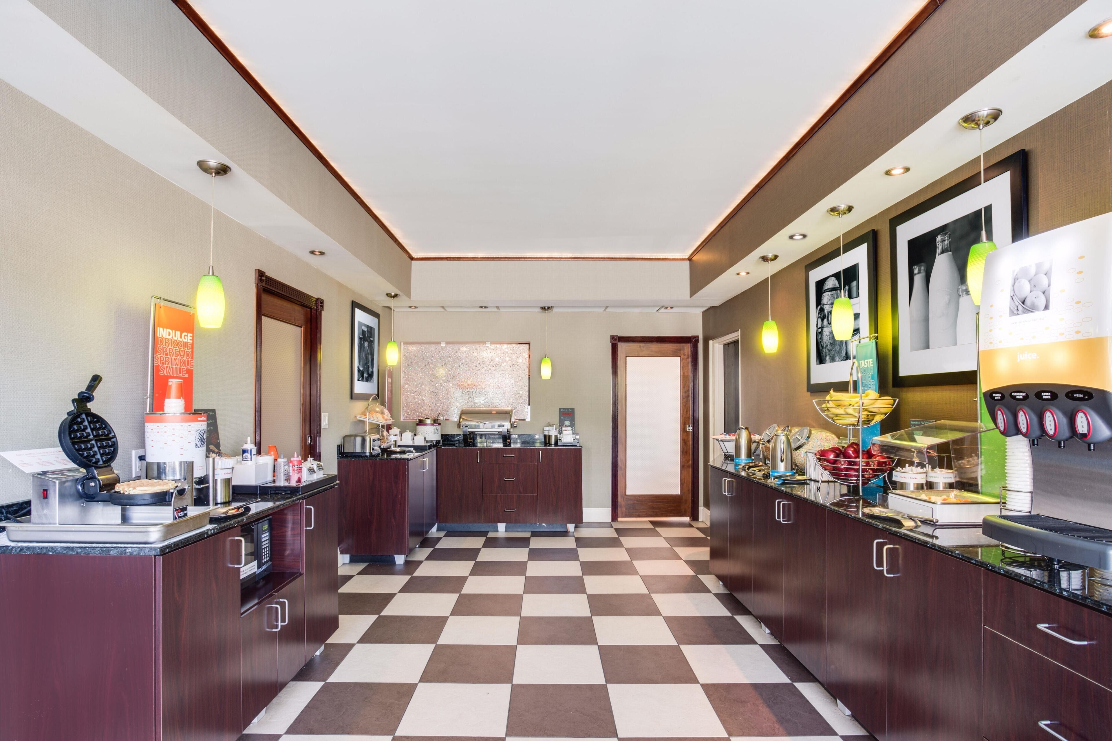 A hotel kitchen with checkered flooring, wooden cabinets, and various kitchen appliances.