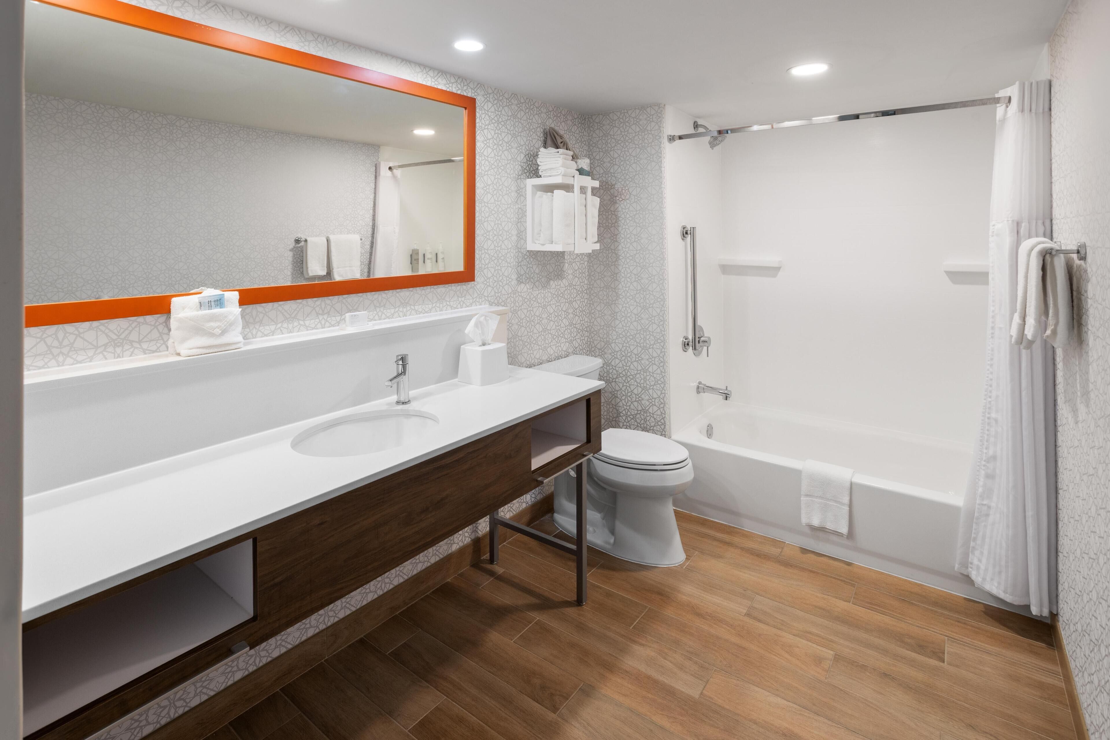 A modern bathroom with a wooden vanity, a large mirror, a toilet, and a shower area.