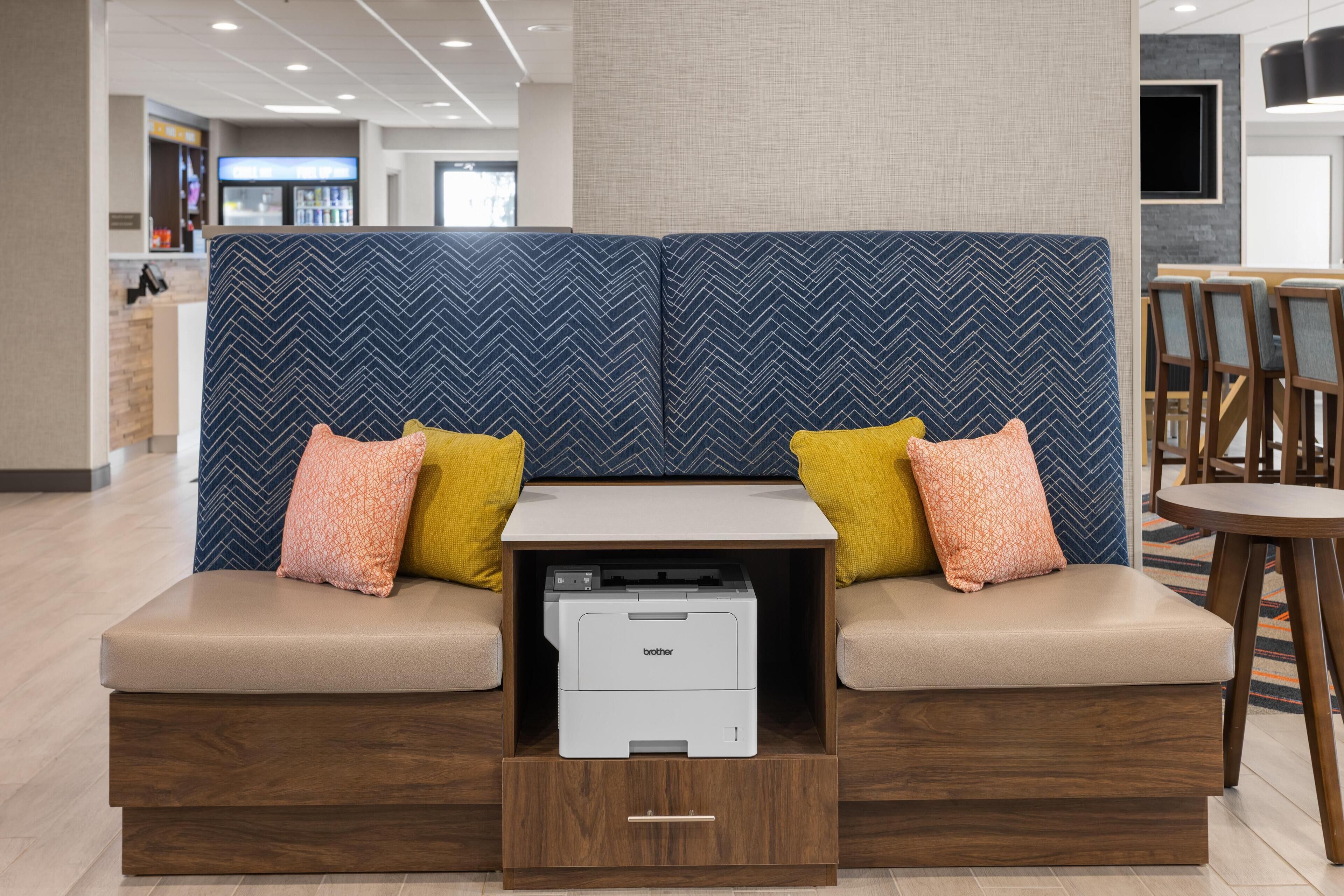 A seating area with a printer, cushioned benches, and a small table.