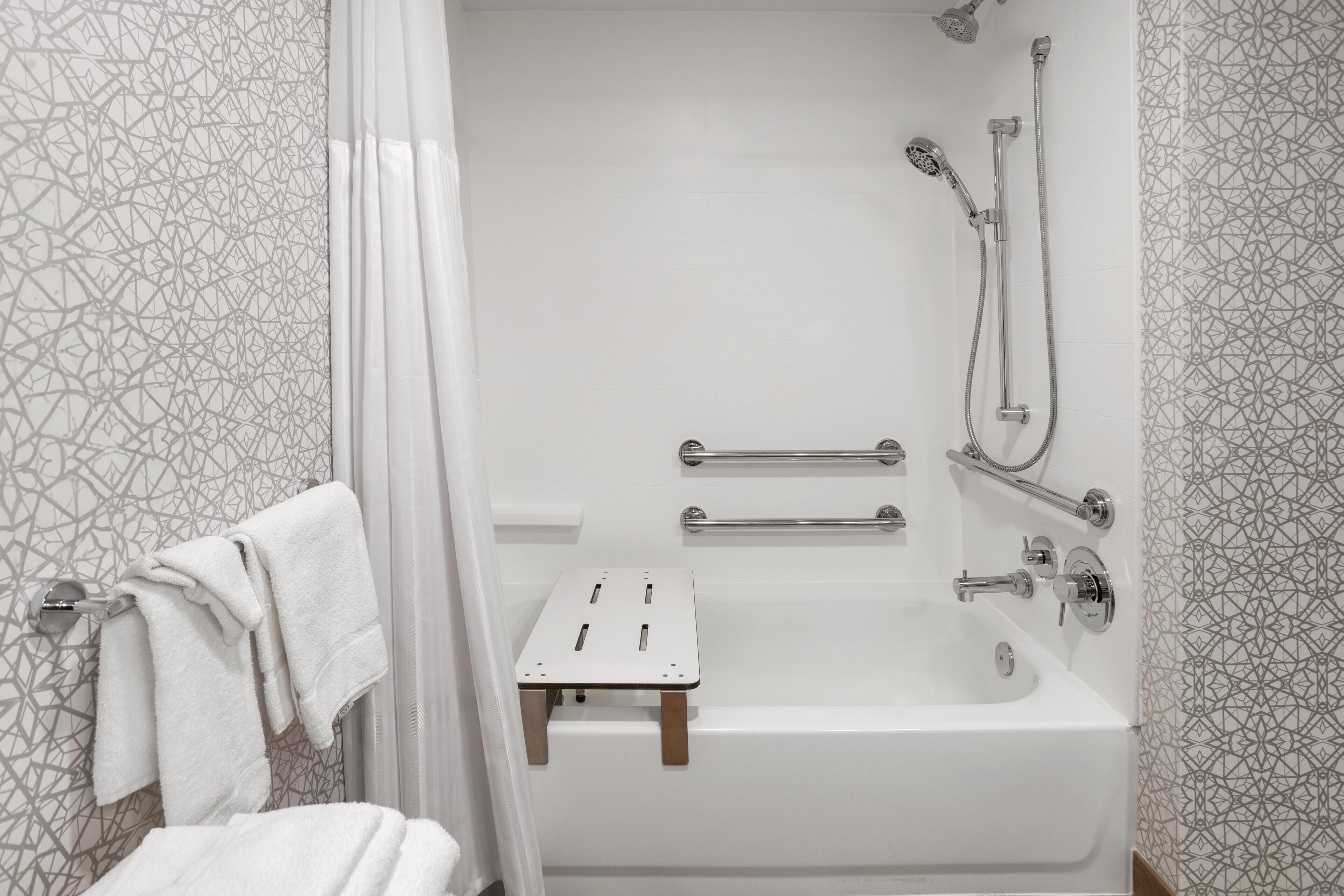 Ein modernes Badezimmer mit Dusche, Haltegriffen und einem kleinen Holzschemel.