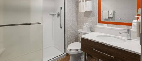 Un baño moderno con cabina de ducha de vidrio, inodoro blanco, tocador de madera con lavamanos y espejo con marco naranja.