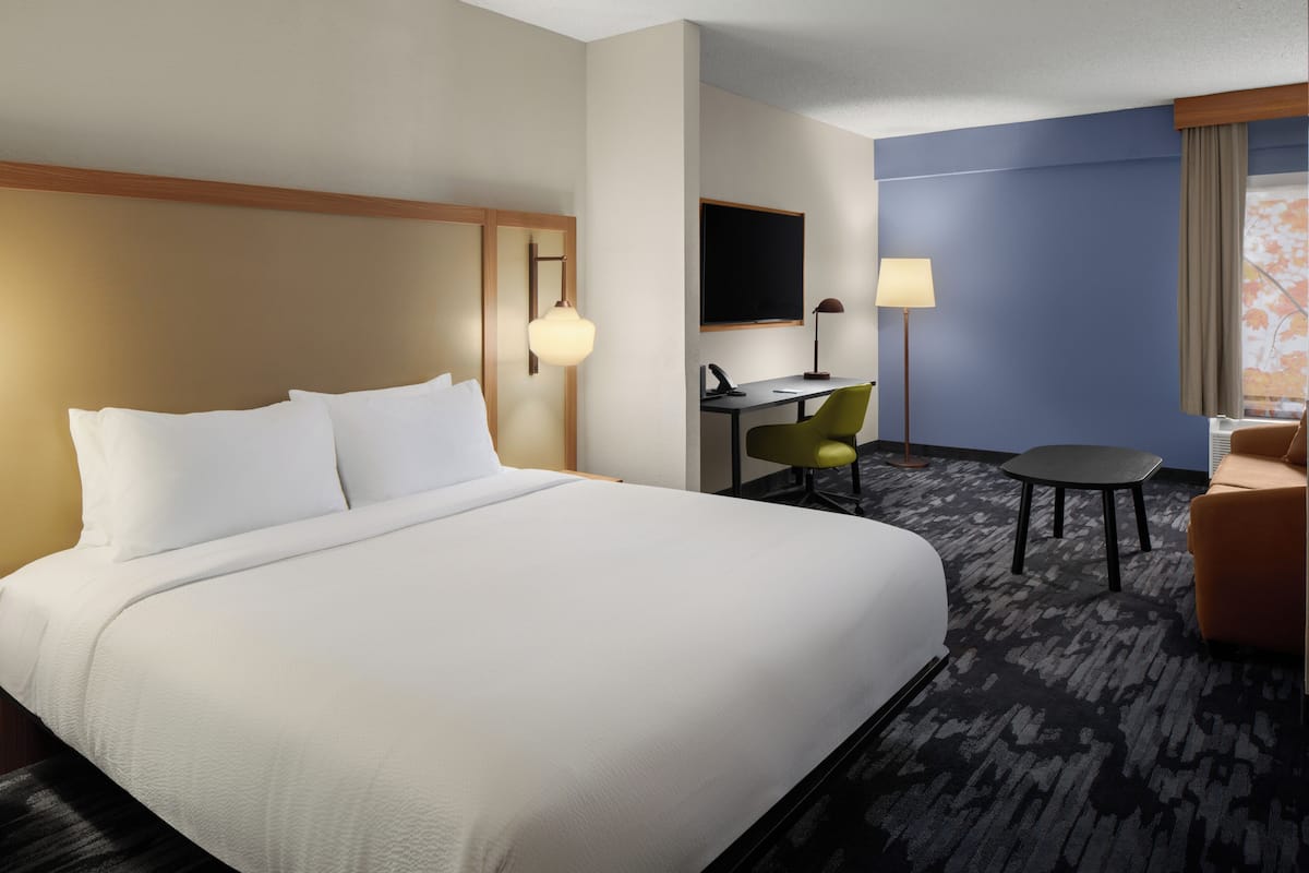 A hotel room with a large bed, a desk with a chair, a small table, and a TV.
