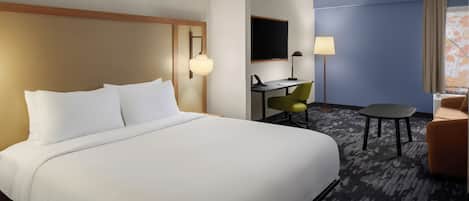 A hotel room with a large bed, a desk with a chair, a small table, and a TV.