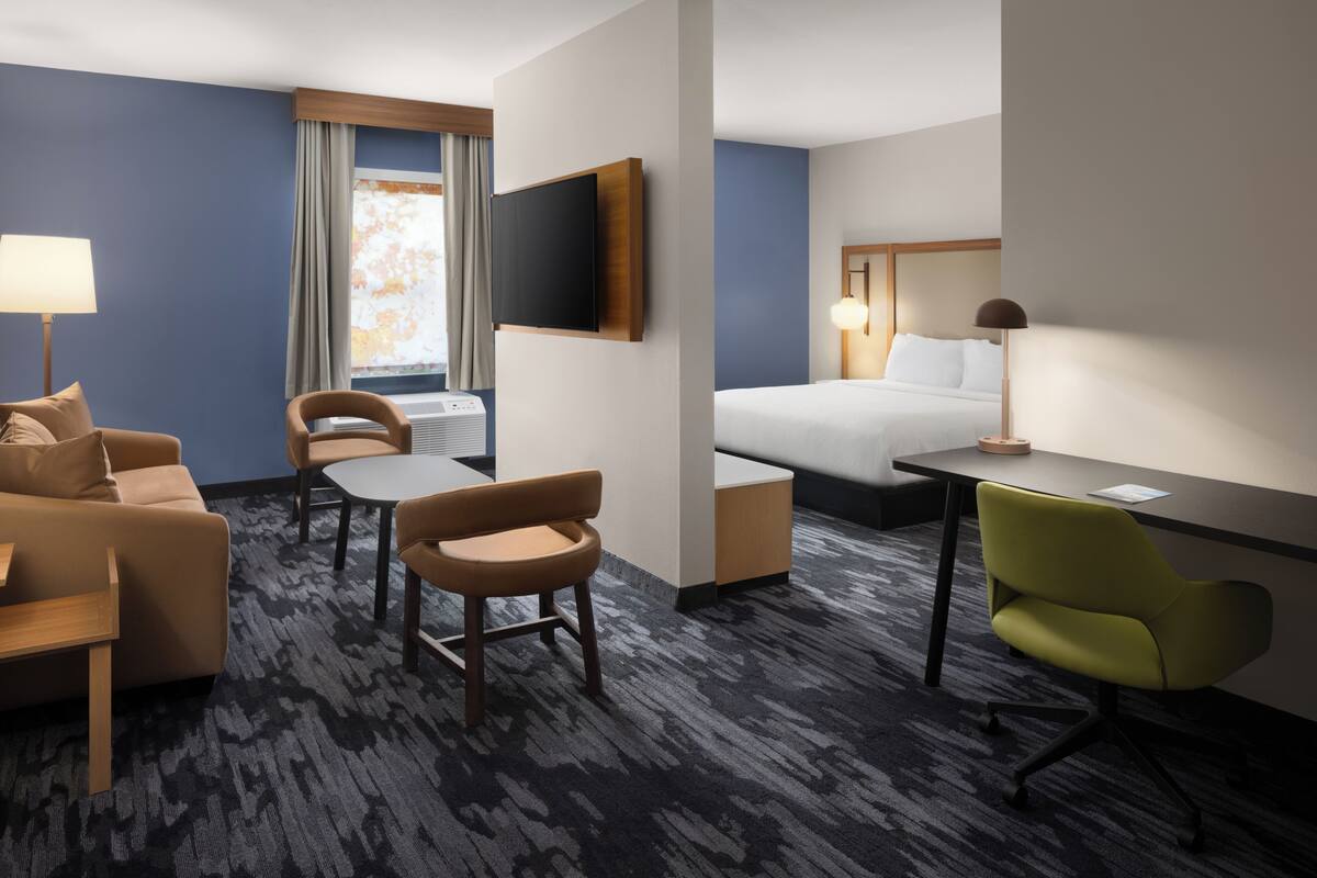 A hotel room with a bed, a desk, a chair, a sofa, and a TV.
