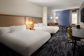 A hotel room with two beds, a desk, a chair, a lamp, and a window.