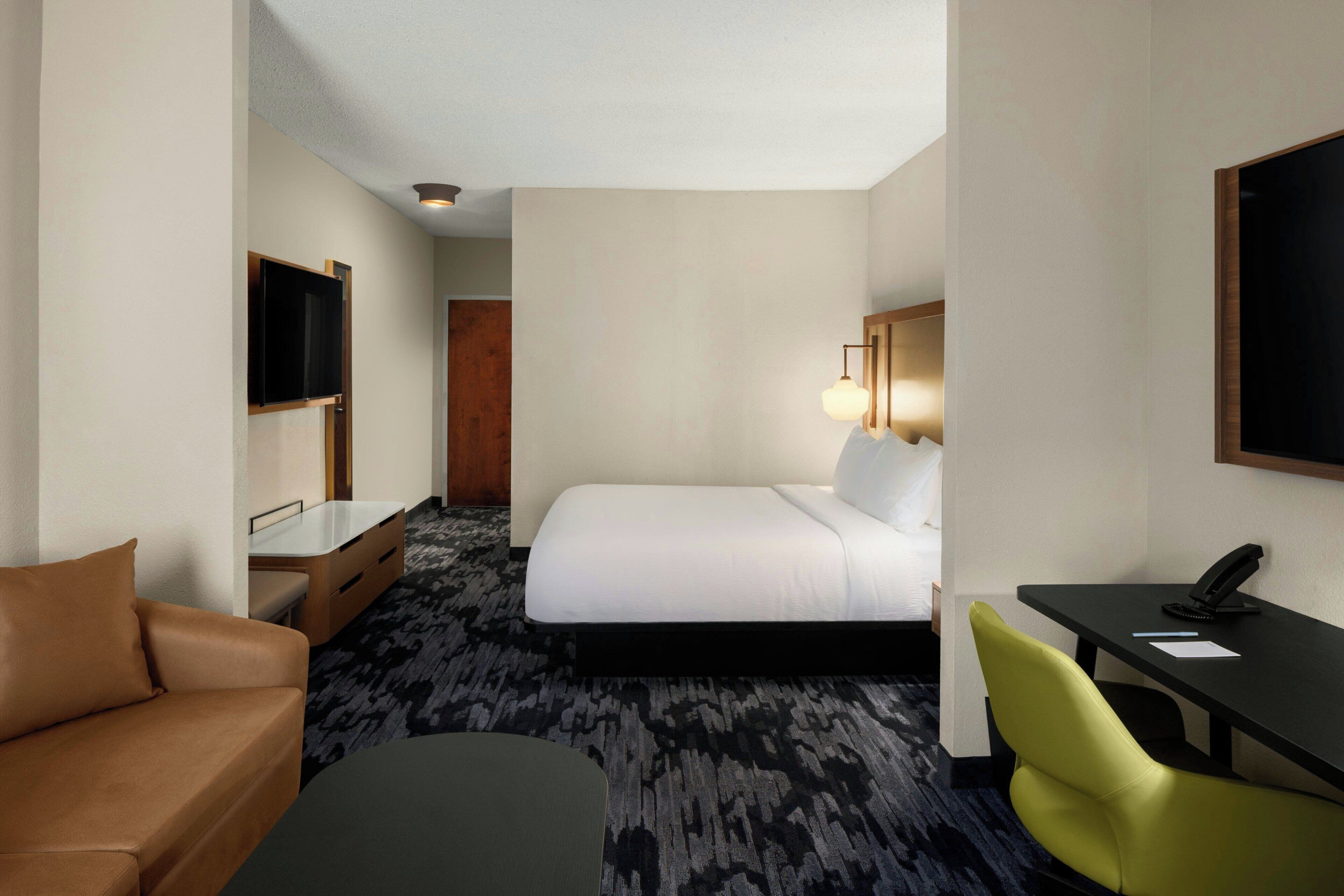 A hotel room with a bed, a desk, a chair, a television, and a lamp.