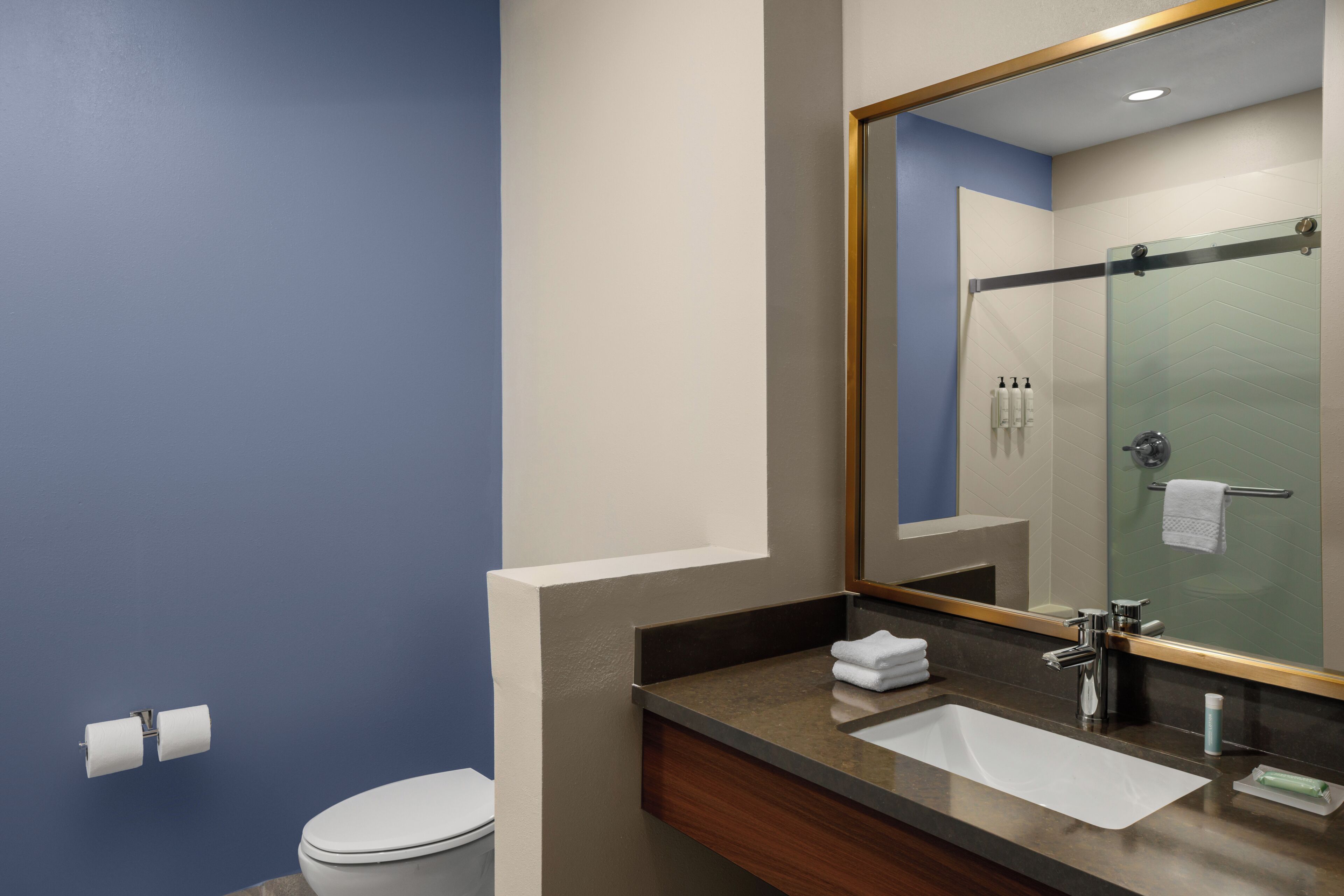 A bathroom with a toilet, sink, mirror, and shower area.