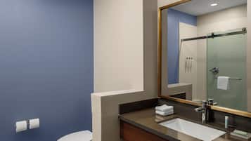 A bathroom with a toilet, sink, mirror, and shower area.