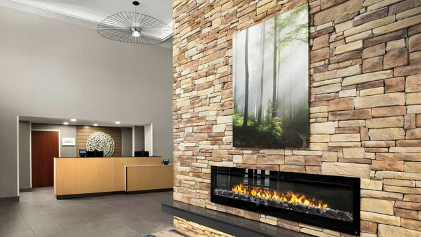 A lobby with a stone wall, a fireplace, a reception desk, and a ceiling light fixture. - Fairfield by Marriott Inn & Suites Columbia Lexington (Lexington)