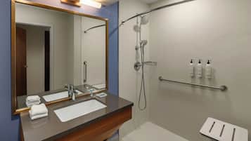 A modern bathroom with a large mirror, a sink, a shower, and a small stool.