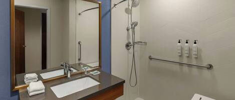 A modern bathroom with a large mirror, a sink, a shower, and a small stool.