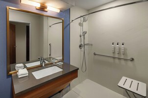 A modern bathroom with a large mirror, a sink, a shower, and a small stool.