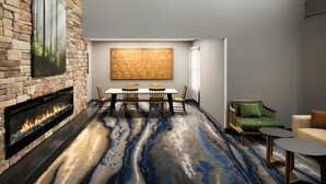 A modern interior with a stone fireplace, a dining table with chairs, a sofa, and a large abstract painting on the wall. - Fairfield by Marriott Inn & Suites Columbia Lexington (Lexington)