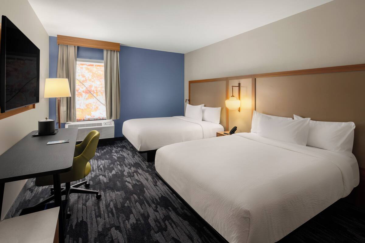 A hotel room with two beds, a desk, a chair, a TV, and a window with curtains.
