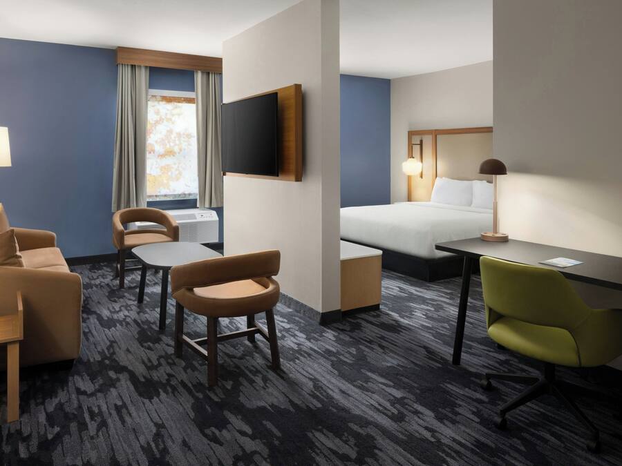A hotel room with a bed, a desk, a chair, a sofa, a TV, and a window with curtains.