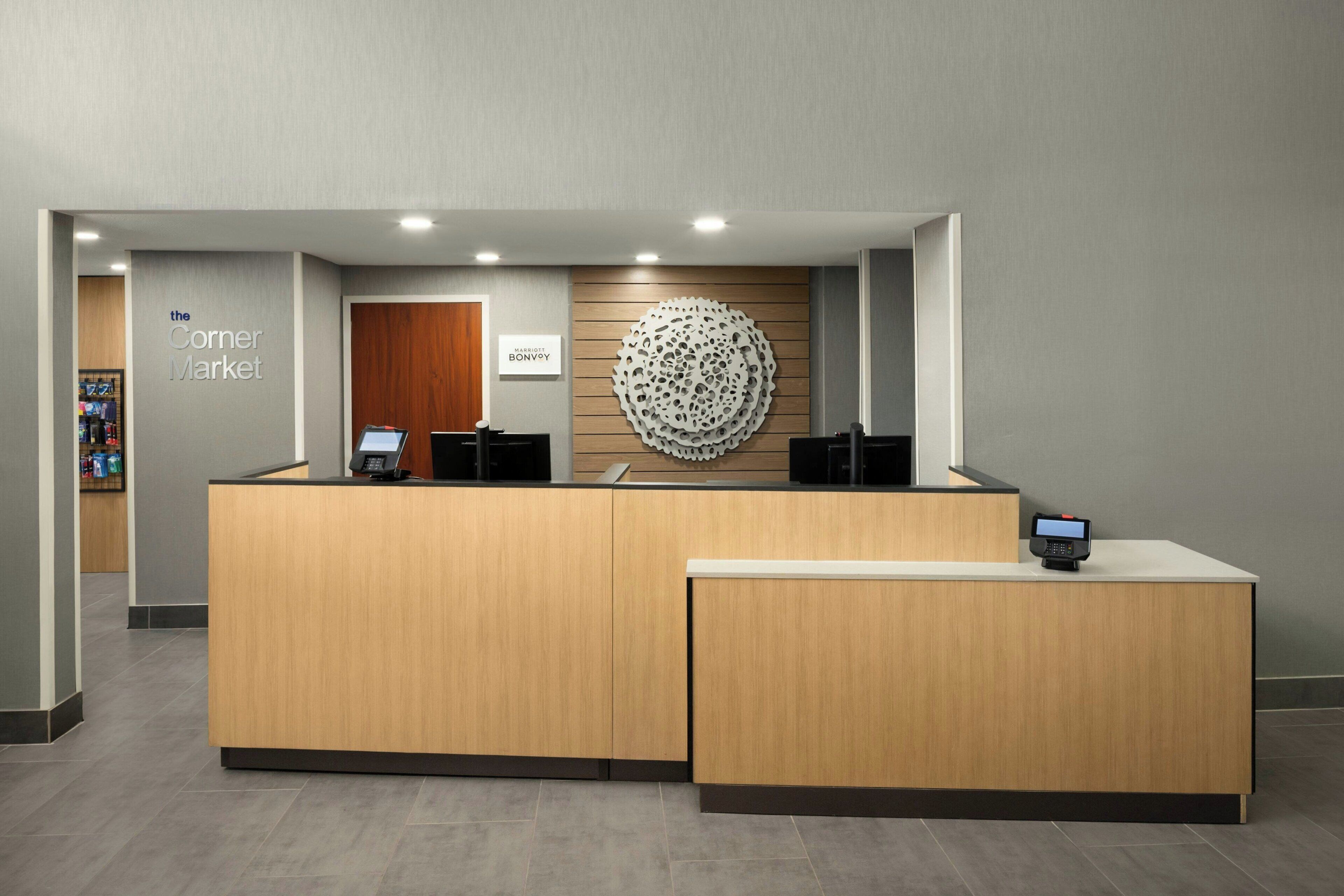 A reception desk with a wooden finish, a logo on the wall, and a digital screen.