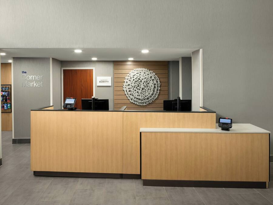 Un mostrador de recepción con detalles de madera, un logotipo en la pared y una pantalla digital.