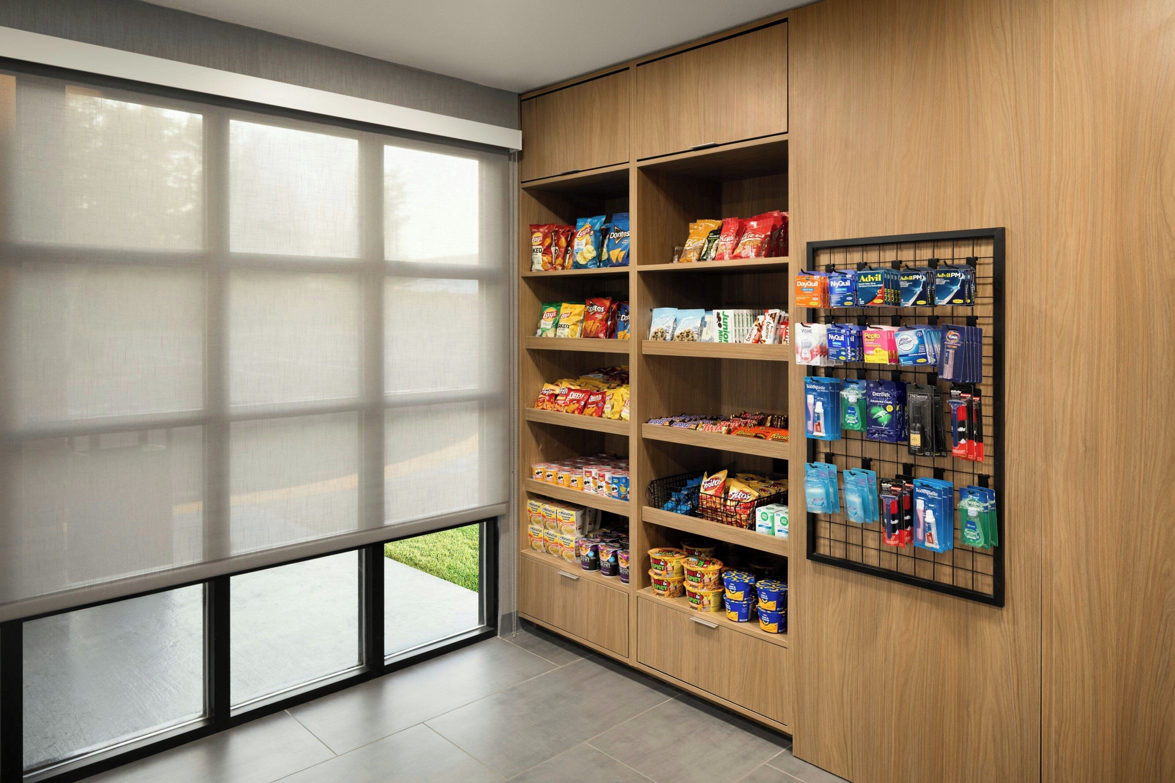 A modern interior with a large window, wooden shelving with snacks and toiletries, and a wall-mounted display.