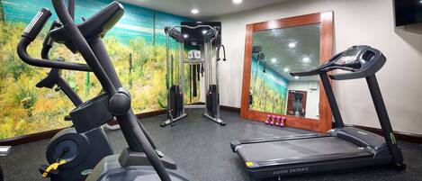 A gym with a treadmill, elliptical, and weight machine, featuring a large mirror and a mural on the wall.
