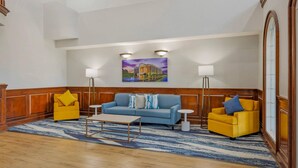 A lobby with a blue sofa, yellow armchairs, a coffee table, and a painting on the wall. - Comfort Suites Sumter near Shaw AFB (Sumter)