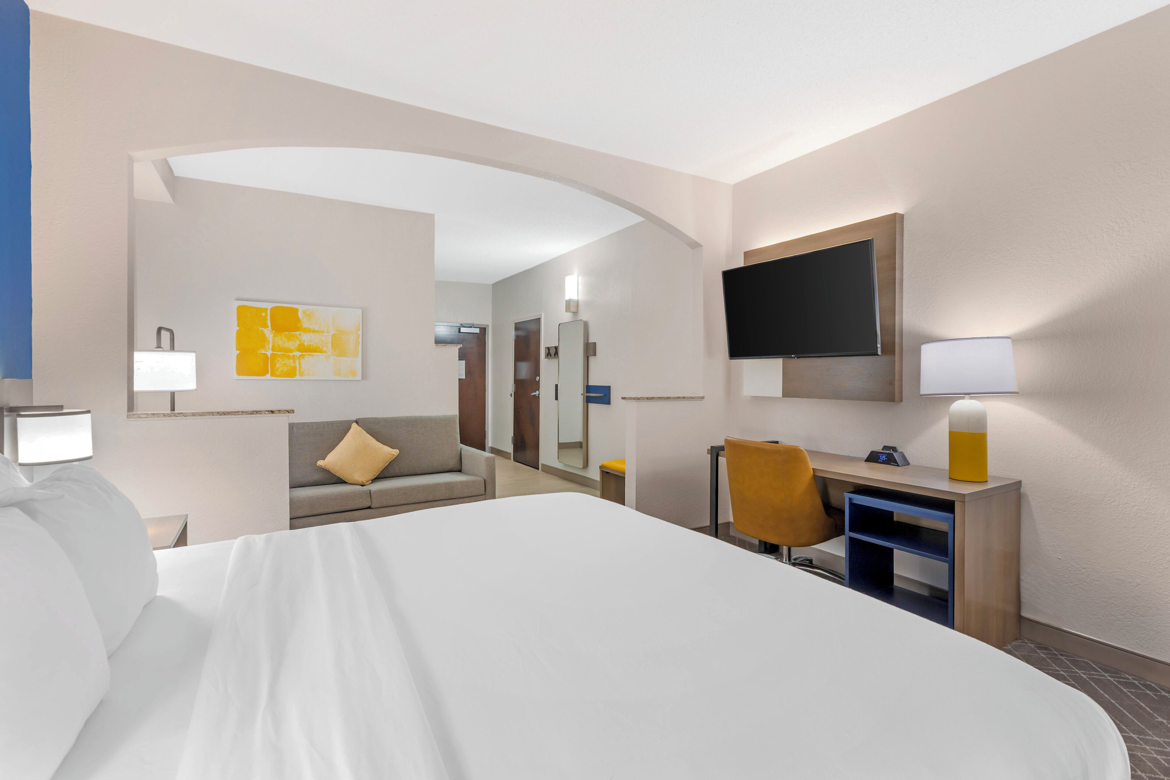 A hotel room with a bed, a desk, a chair, a TV, and a bathroom.