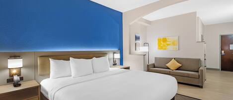 A hotel room with a large bed, a nightstand, a sofa, and a wall with a blue accent.