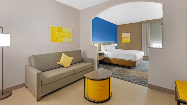 A hotel room with a sofa, a small round table, a bed, and a nightstand. - Comfort Suites Sumter near Shaw AFB (Sumter)