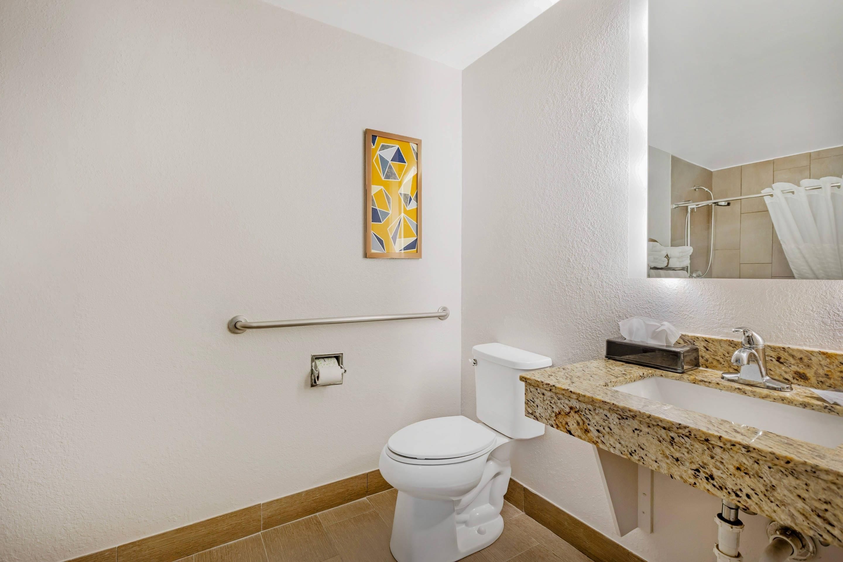 Une salle de bain comprenant des toilettes, un lavabo avec un plan de travail en granit, une barre d’appui et un porte-serviettes.