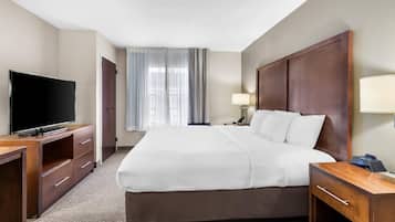 Une chambre d’hôtel avec un grand lit, un téléviseur posé sur un bureau en bois, une table de chevet avec une lampe et une fenêtre avec des rideaux.