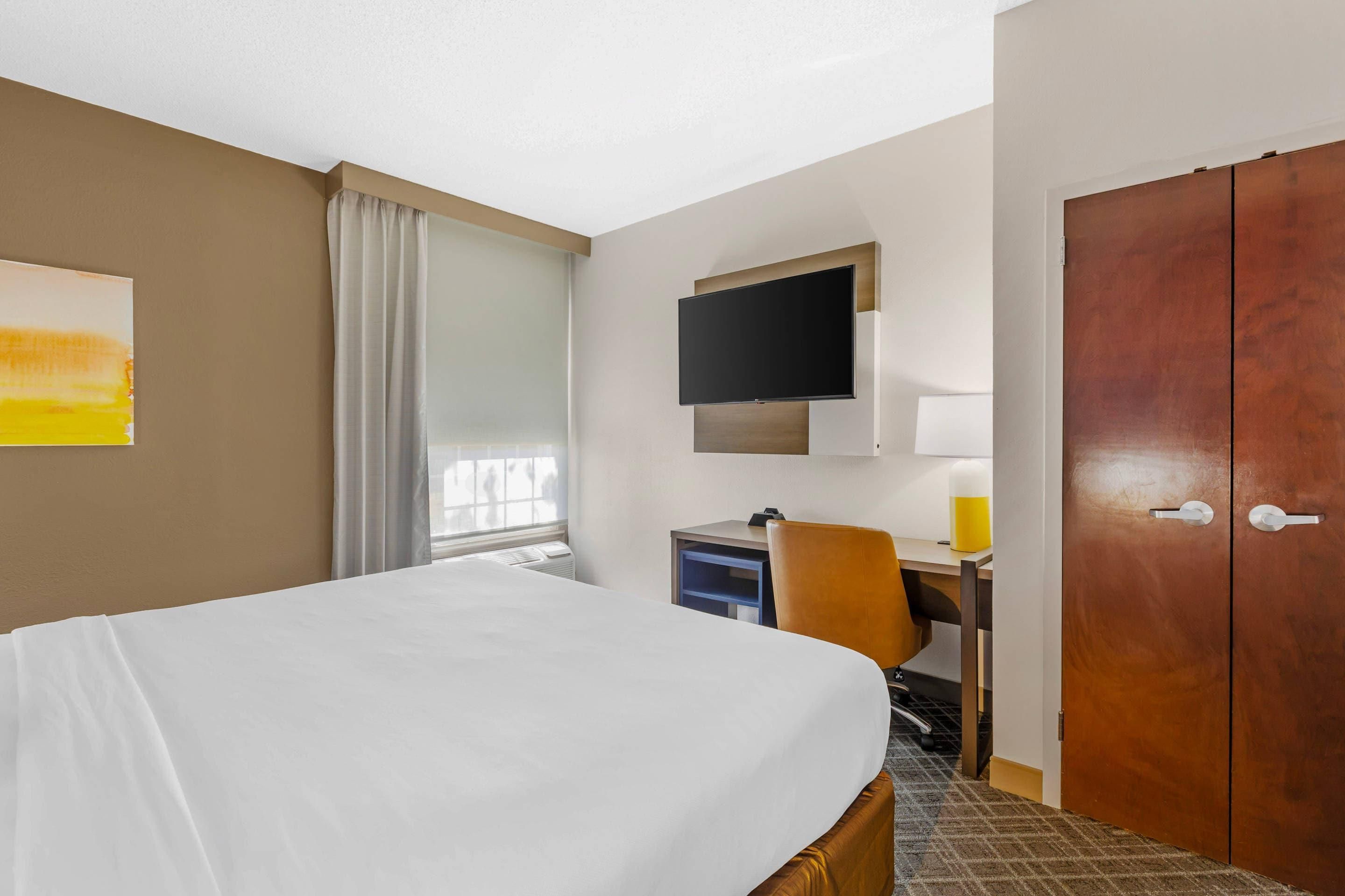 A hotel room with a bed, a desk, a chair, a TV, and a wardrobe.