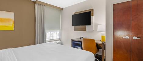 Una habitación de hotel con cama, escritorio, silla, televisor y armario.