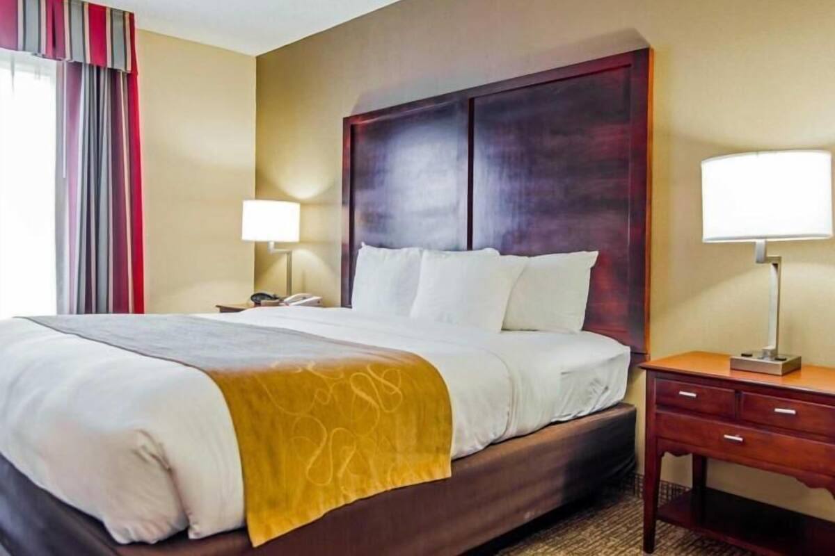 A hotel room with a bed, bedside tables, a lamp, and a window with curtains.